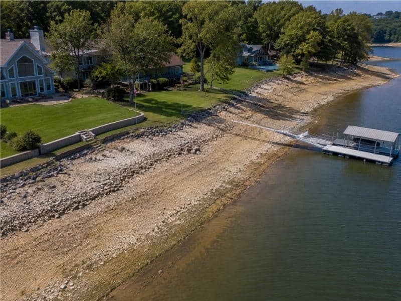 Aerial view of a lakefront lot with exposed shoreline separating the maintained yard from the current waterline.